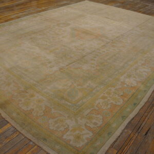Muted traditional rug in beige, pale green, and soft coral colors rests on rustic plank flooring.