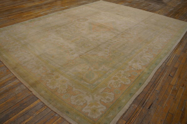 Muted traditional rug in beige, pale green, and soft coral colors rests on rustic plank flooring.
