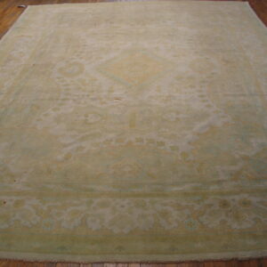 Large traditional rug with faded sage green and tan colors covers a rich brown wood floor.