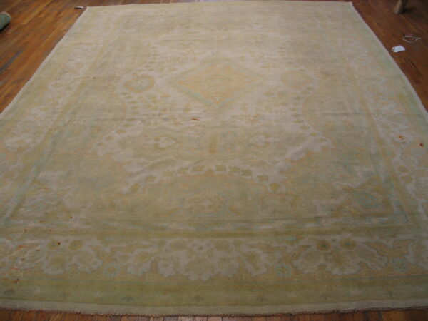 Large traditional rug with faded sage green and tan colors covers a rich brown wood floor.