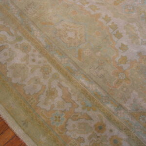 Muted traditional rug with floral and medallion motifs in soft green and gold rests on hardwood floors.