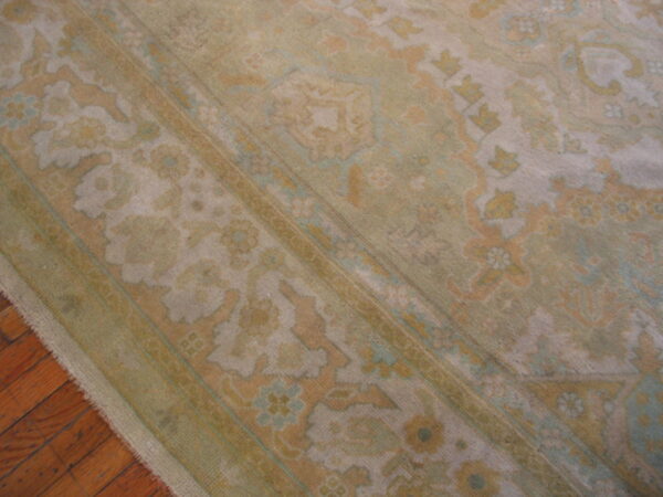Muted traditional rug with floral and medallion motifs in soft green and gold rests on hardwood floors.
