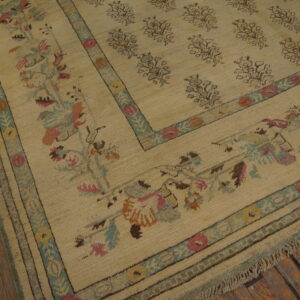 Textured beige area rug featuring repeating field motifs and a detailed border in pink, teal, orange, and brown.