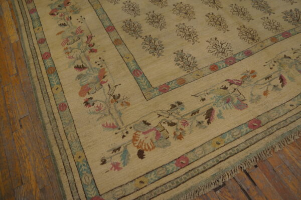 Textured beige area rug featuring repeating field motifs and a detailed border in pink, teal, orange, and brown.