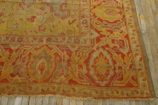 A corner section of a gold and red patterned rug with low pile lying on distressed light wood floors.