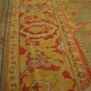 Low-pile rug with red and golden traditional patterns rests beside distressed wide plank flooring.