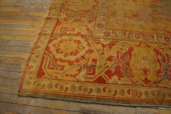 Gold and red patterned shag rug with fringes resting on distressed, light wood flooring.