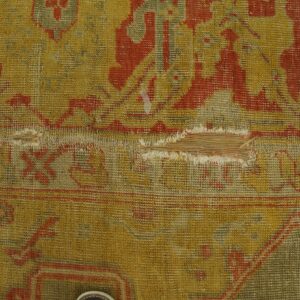 Mustard yellow and rust red patterned rug with heavy wear and a large horizontal tear.