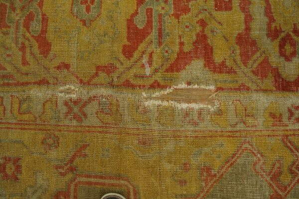 Mustard yellow and rust red patterned rug with heavy wear and a large horizontal tear.