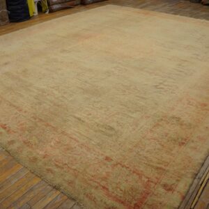 Large beige rug with faint coral and green patterns rests on distressed wooden floorboards.