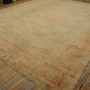 Oversized distressed rug with faded cream and pink traditional patterns covers narrow wood plank flooring.
