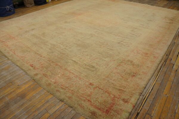Oversized distressed rug with faded cream and pink traditional patterns covers narrow wood plank flooring.