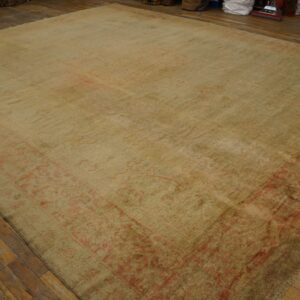 Low-pile area rug in pale olive and faded red with an ornate border on distressed plank wood flooring.
