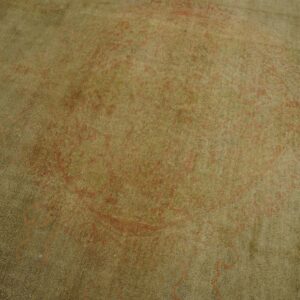 Soft pile rug detail showing faint red-orange traditional patterns over a muted olive green field.