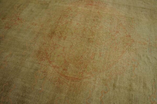 Soft pile rug detail showing faint red-orange traditional patterns over a muted olive green field.