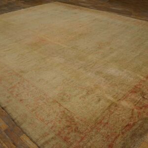 Large beige rug with a muted red patterned border on rustic, dark wood plank flooring.