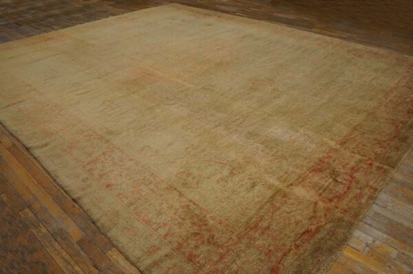 Large beige rug with a muted red patterned border on rustic, dark wood plank flooring.