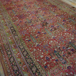 Intricate red rug with green and blue botanical patterns resting on rustic wood flooring.