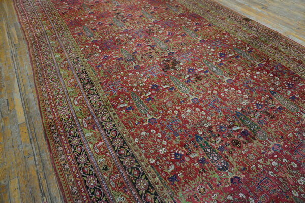 Intricate red rug with green and blue botanical patterns resting on rustic wood flooring.