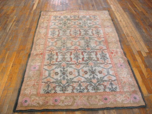 Traditional beige and pink rug with a floral trellis pattern lying on wide plank hardwood flooring.