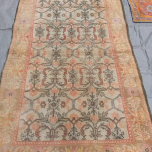 Light beige rug with a repeating coral, taupe, and gray floral trellis pattern displayed on a gray cloth.