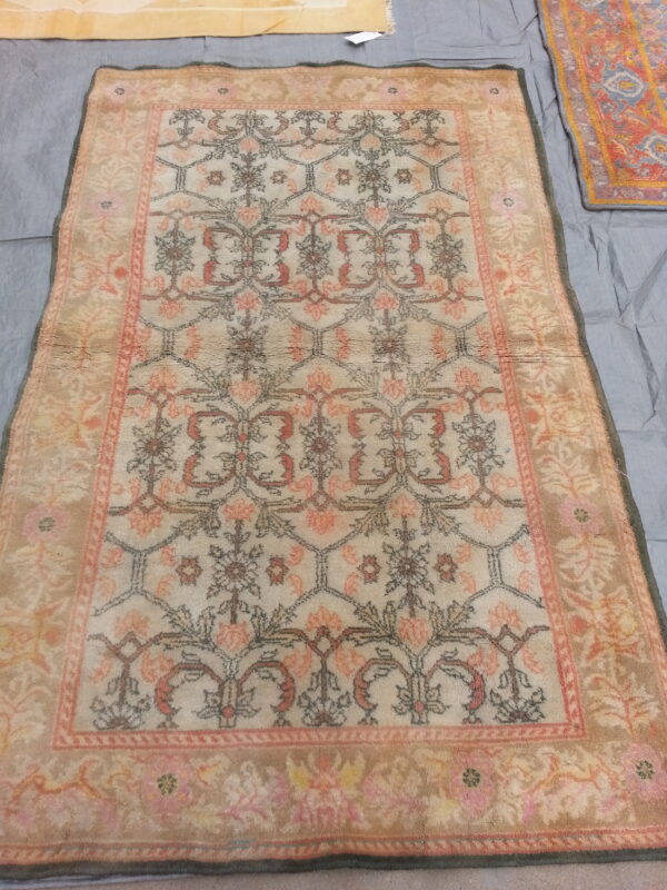 Light beige rug with a repeating coral, taupe, and gray floral trellis pattern displayed on a gray cloth.