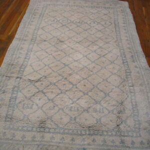 Textured cream rug with a blue trellis pattern and borders rests on reddish-brown hardwood flooring.