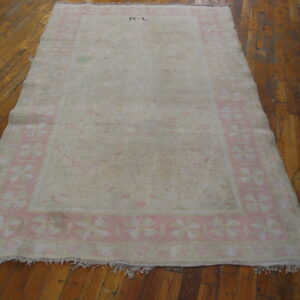 Distressed cream rug with a pale pink floral border and R L initials rests on wood planks.