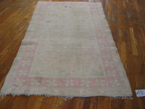 Distressed cream rug with a pale pink floral border and r l initials rests on wood planks.