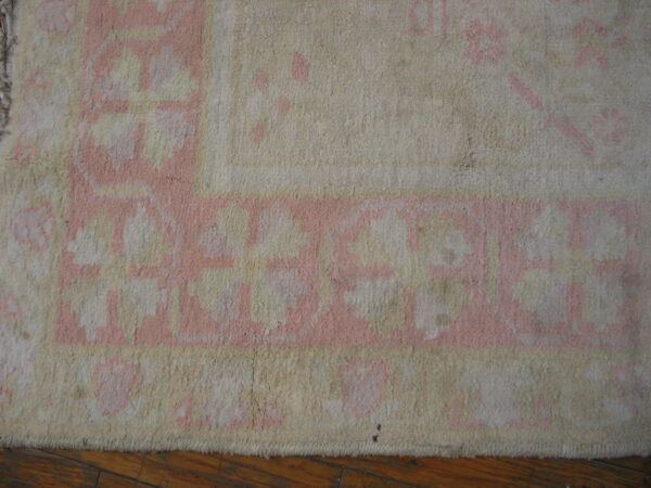 A cream and rose border pattern is visible on a textured pile rug resting on wood planks.