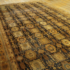 Large black rug with gold repeating geometric medallion patterns lying on natural wood flooring.