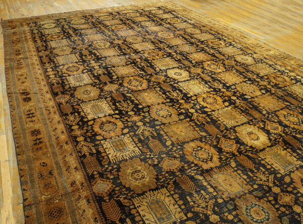 Large black rug with gold repeating geometric medallion patterns lying on natural wood flooring.