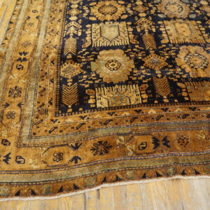 Gold and dark blue geometric rug with a wide border lying on light wood planks.