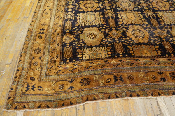 Gold and dark blue geometric rug with a wide border lying on light wood planks.