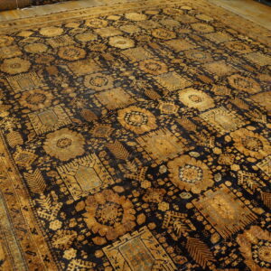 Intricate gold geometric and floral patterns cover a dark blue rug laid on rustic wood floors.