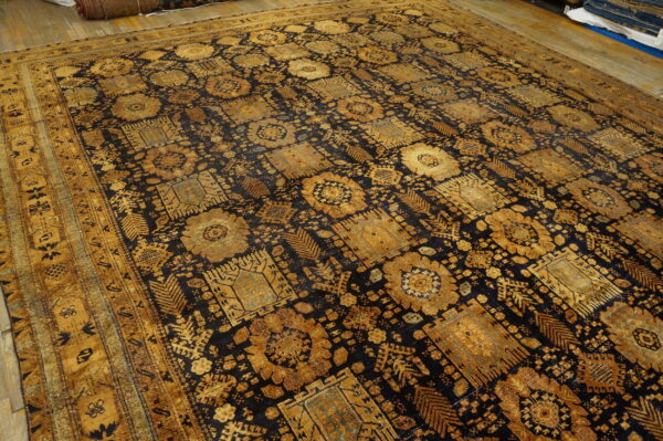 Intricate gold geometric and floral patterns cover a dark blue rug laid on rustic wood floors.