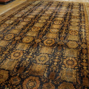 Dark navy and golden traditional rug with repeating motifs displayed on light wood plank flooring.