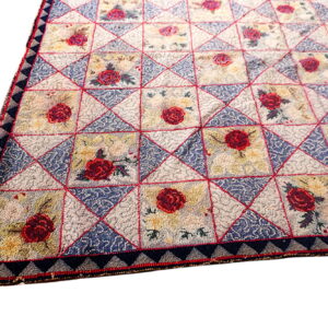 A textured rug with a quilt-like pattern of squares featuring red roses and blue patterned triangles.