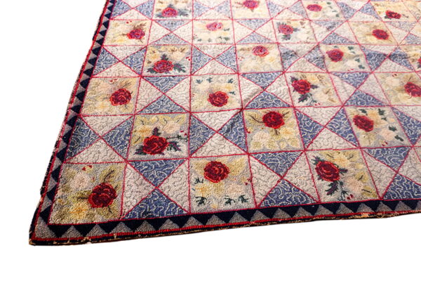 A textured rug with a quilt-like pattern of squares featuring red roses and blue patterned triangles.