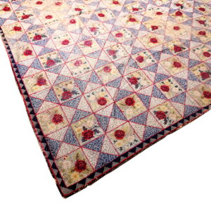 A low-pile rug with a geometric pattern of red roses, blue triangles, and cream floral squares.