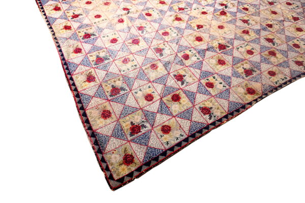 A low-pile rug with a geometric pattern of red roses, blue triangles, and cream floral squares.