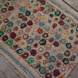 A textured rug with a scattered pattern of multicolored circles lies diagonally on distressed gray wood.