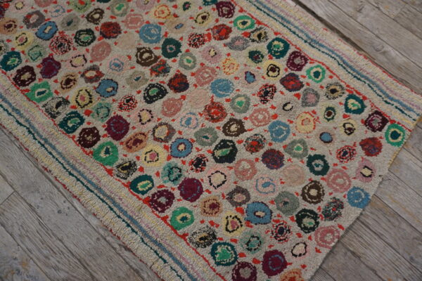 A textured rug with a scattered pattern of multicolored circles lies diagonally on distressed gray wood.