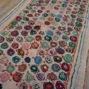 A high-pile runner rug with multicolored circular motifs rests upon light gray distressed wood plank flooring.