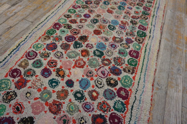 A high-pile runner rug with multicolored circular motifs rests upon light gray distressed wood plank flooring.