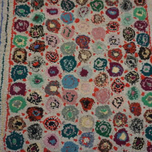 Multicolor looped rug with bright, irregular floral motifs and a shaggy pile rests on wood flooring.