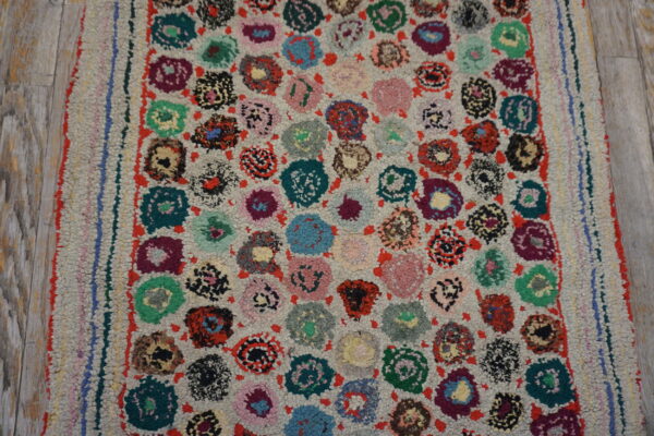 Multicolor looped rug with bright, irregular floral motifs and a shaggy pile rests on wood flooring.