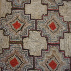 Close-up of a highly textured rug with cream crosses and multicolor diamonds, next to gray wooden planks.