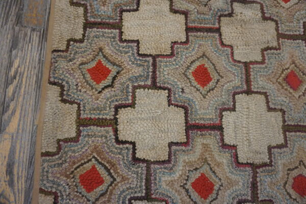 Close-up of a highly textured rug with cream crosses and multicolor diamonds, next to gray wooden planks.