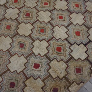 A rustic, heavily textured rug featuring beige and red geometric motifs on gray wood flooring.